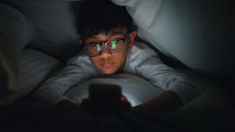 Close-Up-Of-Young-Boy-In-Bedroom-At-Home-Using-Mobile-Phone-To-Text-Message-Under-Covers-Or-Duvet-At-Night-7